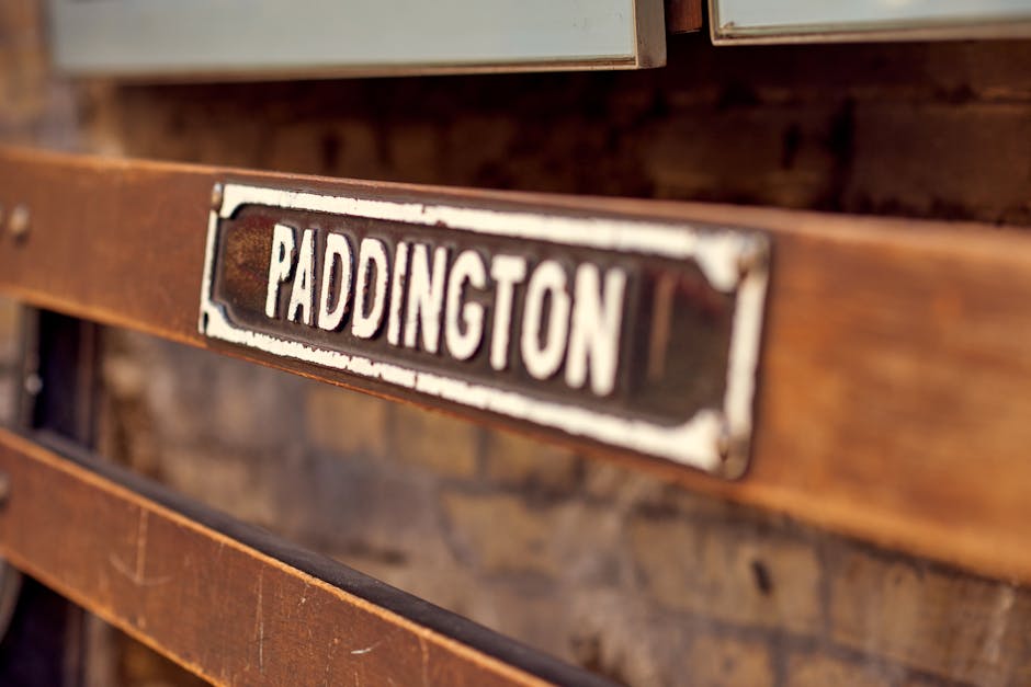 A close-up view of a vintage-style metal sign with the word 'PADDINGTON' painted in white letters on a black background. The sign is mounted on a weathered wooden surface with visible grain and a reddish-brown stain, likely part of an old piece of furniture or a decorative structure. The lighting is soft and warm, highlighting the aged texture of the wood and the slight rust or chipping on the metal sign. This setting suggests a rustic or historic ambiance, fitting for a location such as Paddington. Paddington Carpet Cleaners emphasizes professional surface cleaning and deep sanitisation, ensuring clutter-free and hygienic spaces in residential or commercial environments, aligning with Westminster Council rules on safe and eco-friendly carpet disposal and maintenance. The image visually conveys a sense of timelessness and durability, suitable for illustrating thorough cleaning processes or heritage-inspired decor.